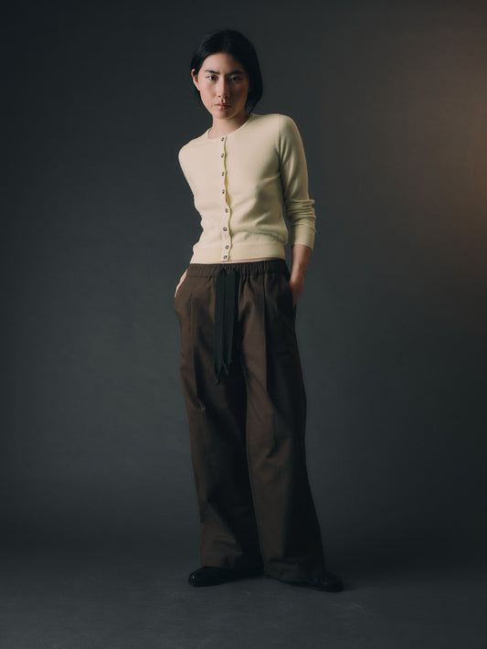 Woman wearing a light yellow cashmere cardigan and brown pants against a dark background