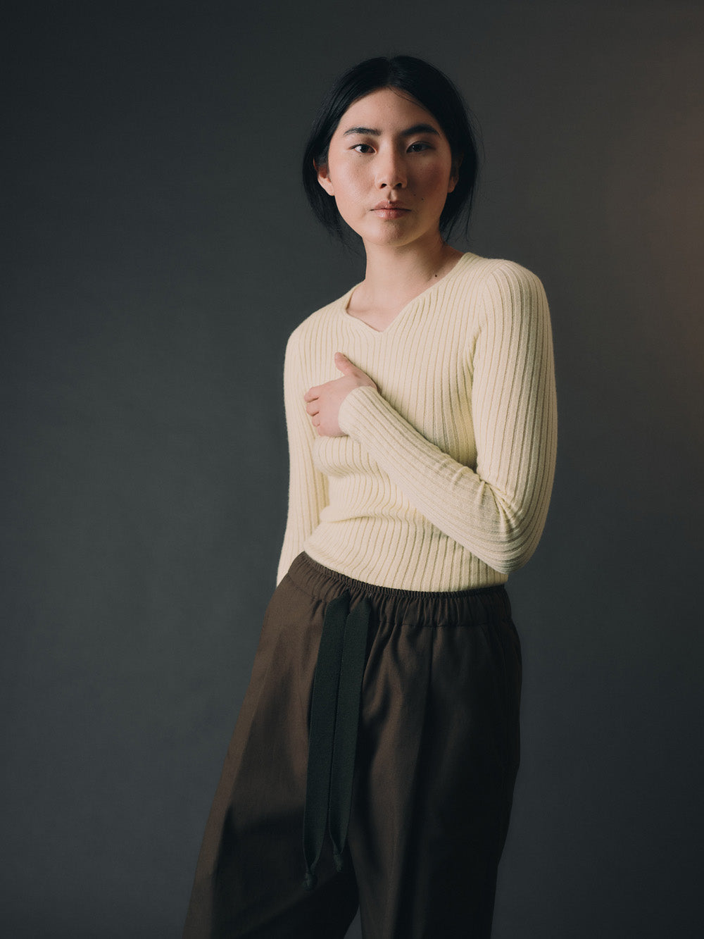 Woman wearing a light yellow cashmere sweater and dark pants against a gray background
