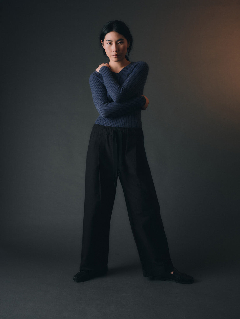 Woman wearing a blue cashmere sweater and dark pants against a gray background
