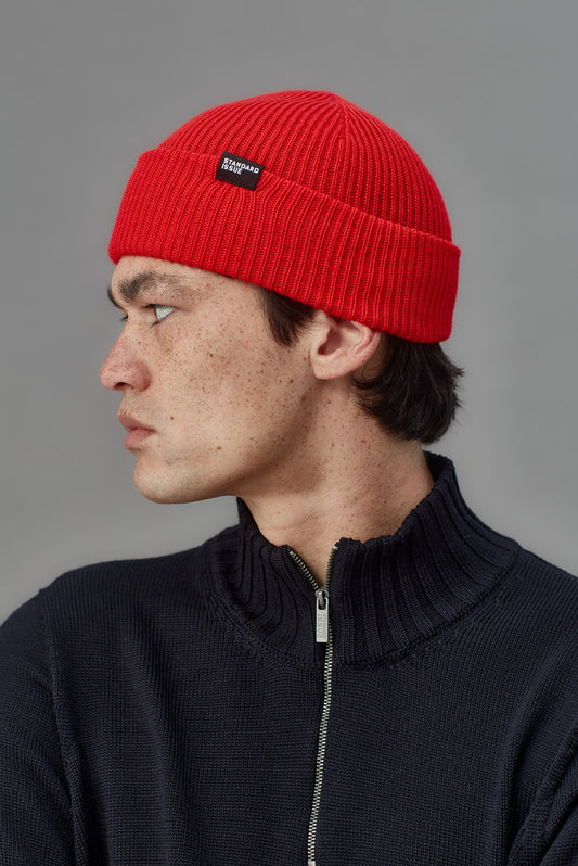 Person wearing a red beanie with a logo on a gray background