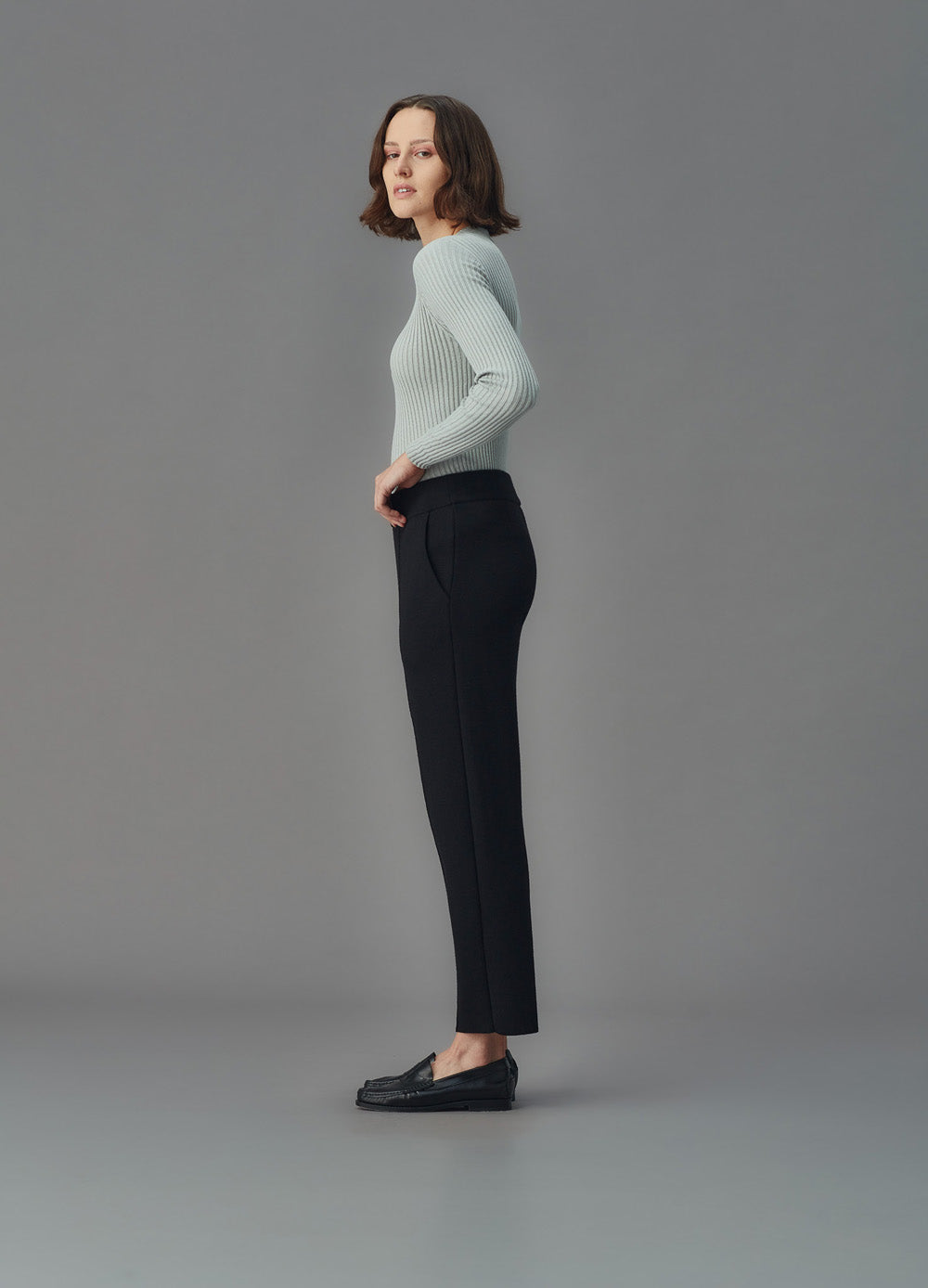 Woman wearing black merino pants and a light blue sweater against a gray background