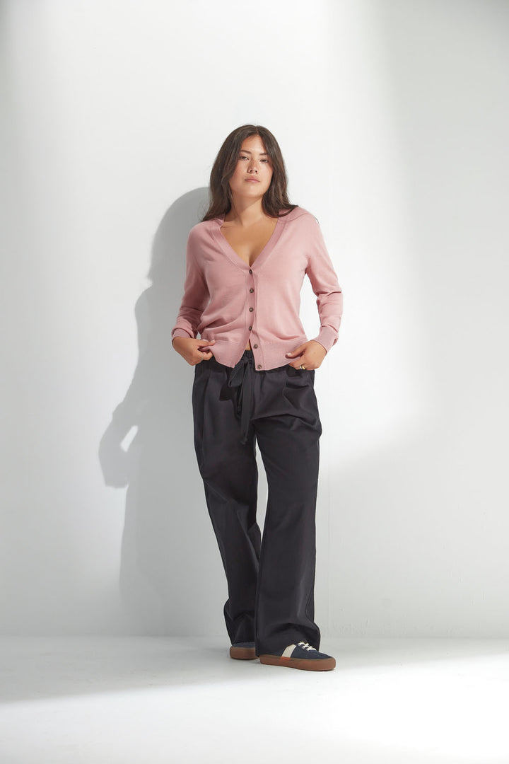 Woman wearing a pink cardigan and dark pants against a white background