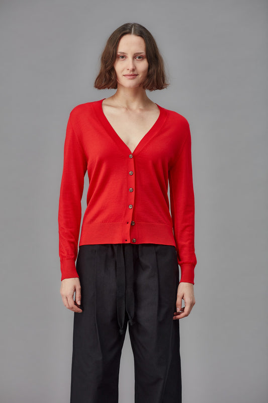 Woman wearing a red cardigan and black pants against a gray background