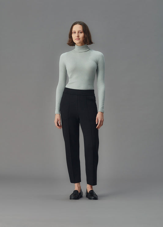 Woman wearing a light blue ribbed top and black pants against a gray background