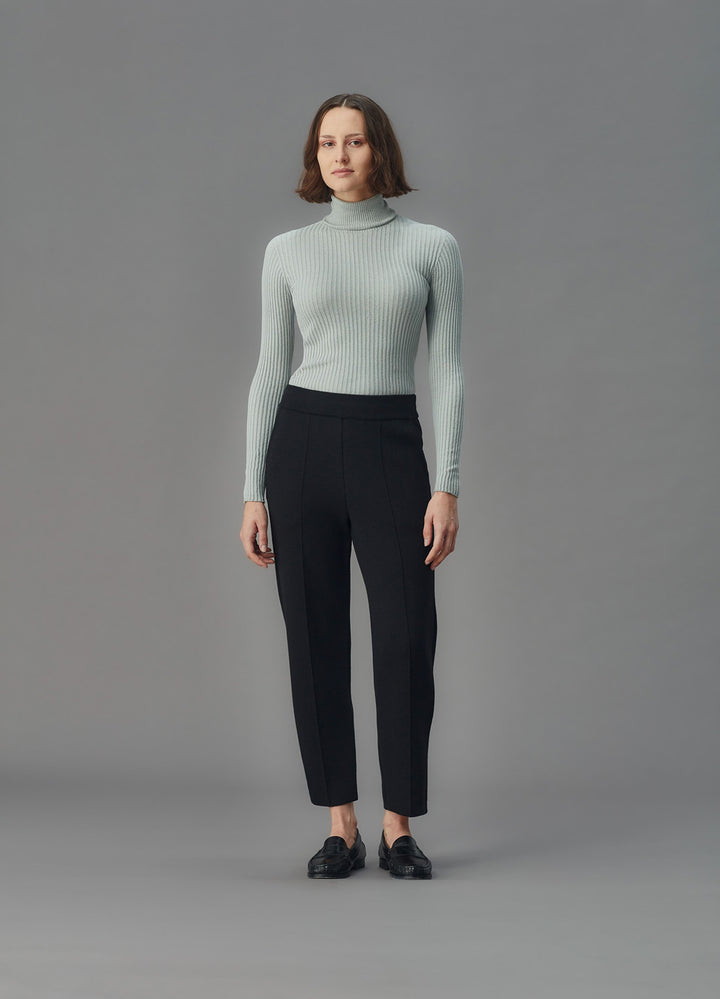 Woman wearing a light blue ribbed top and black pants against a gray background