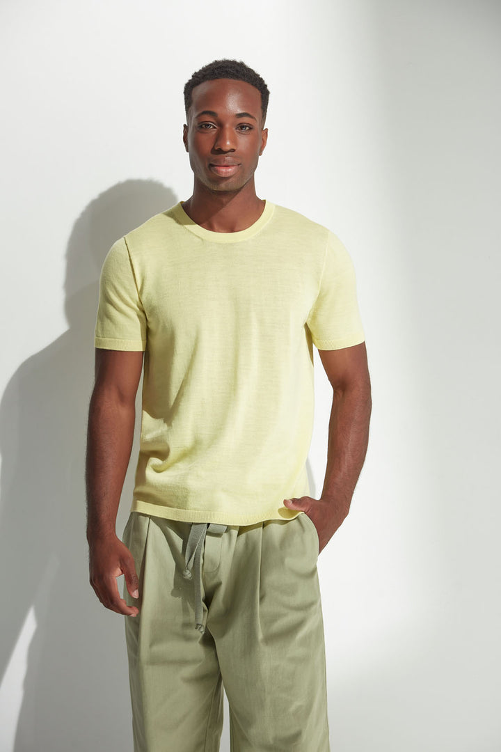 Man wearing a light yellow t-shirt and green pants against a white background