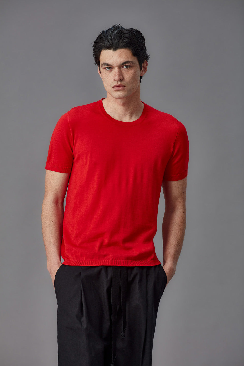 Man wearing a red merino shirt and black pants against a gray background