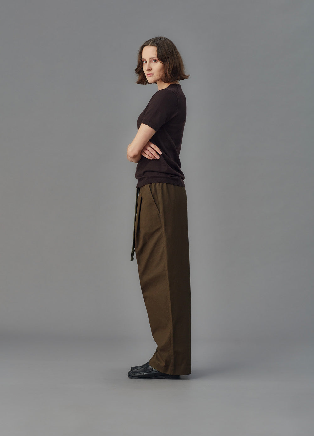 Women wearing a brown merino shirt and brown pants standing against a gray background