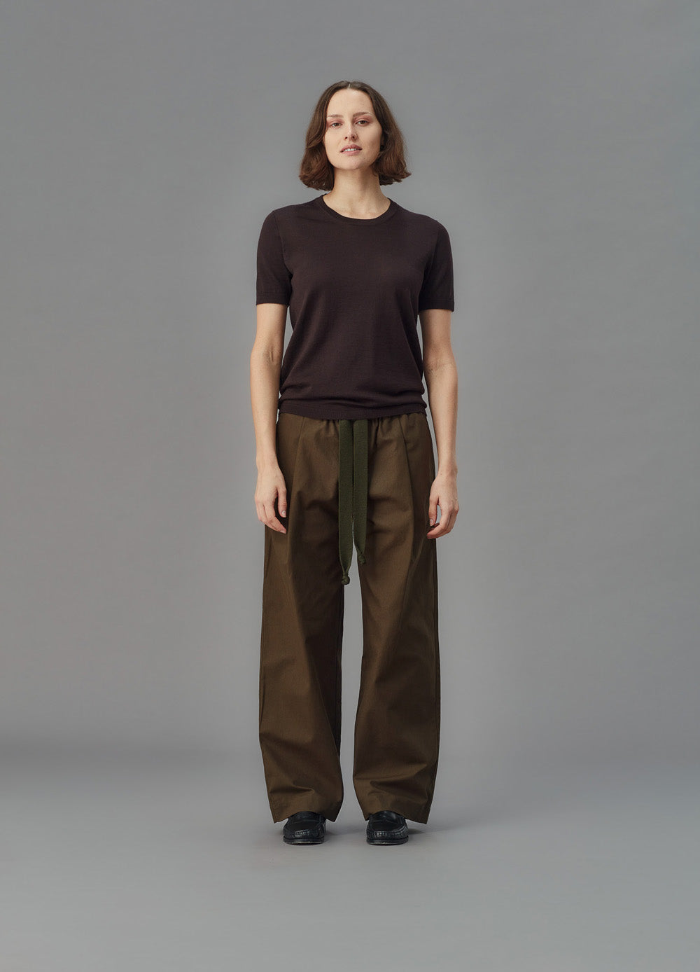 Women wearing a brown merino shirt and brown pants standing against a gray background