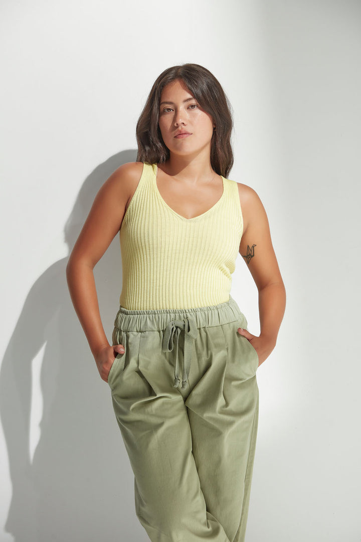 Woman wearing a yellow tank top and green pants against a white background