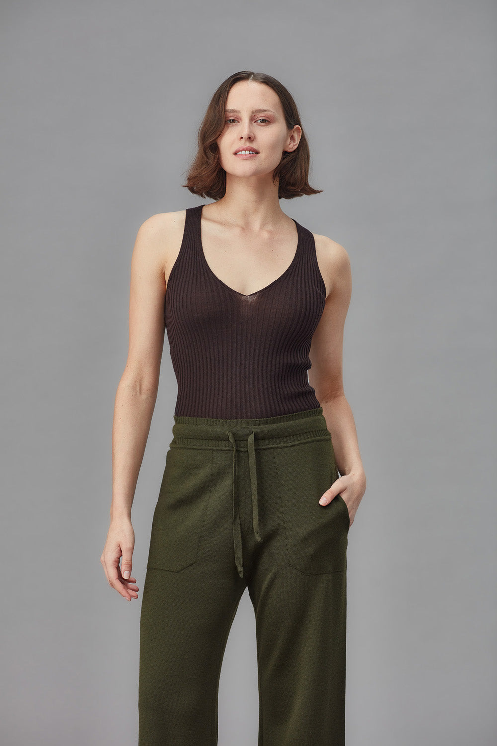 Woman wearing a brown ribbed tank top and green pants against a gray background