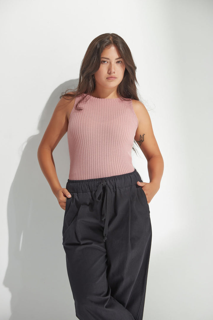 Woman wearing a pink sleeveless top and dark pants against a white background