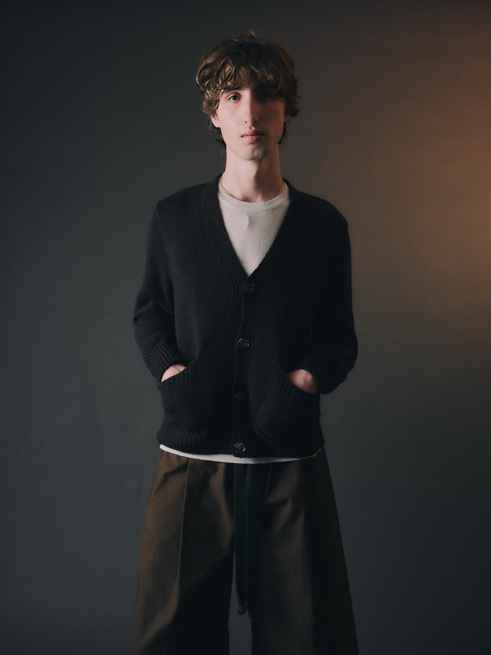 Person wearing a dark cardigan over a white shirt on a dark background