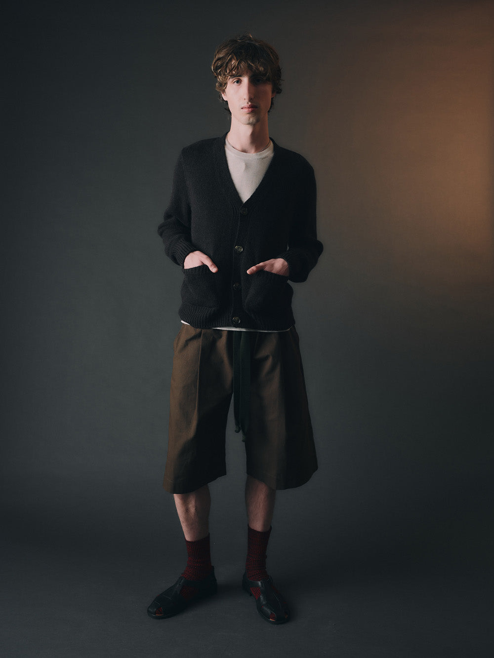 Person wearing a dark cardigan, light shirt, and green shorts against a plain background