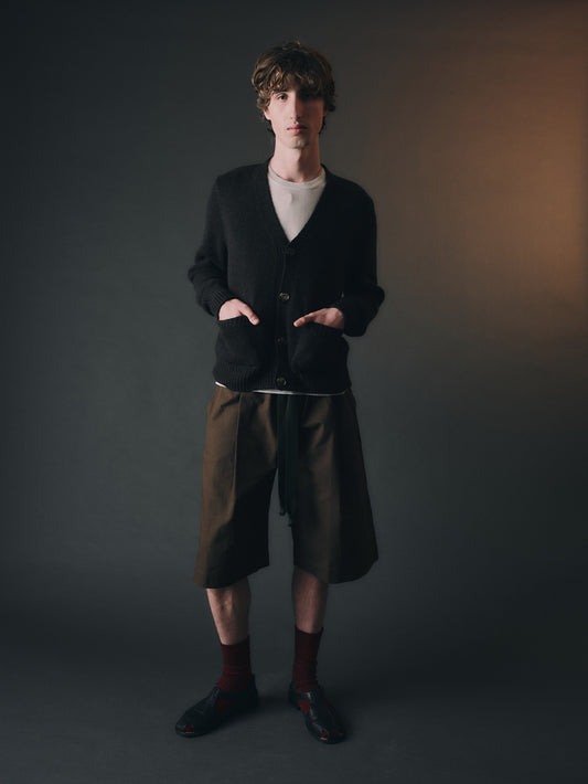 Person wearing a dark cardigan, light shirt, and green shorts against a plain background