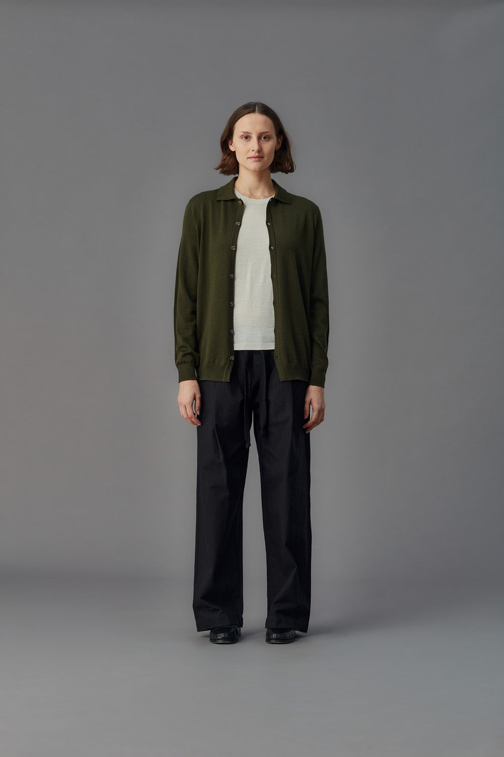 Person wearing a green shirt over a white shirt, and black pants on a gray background