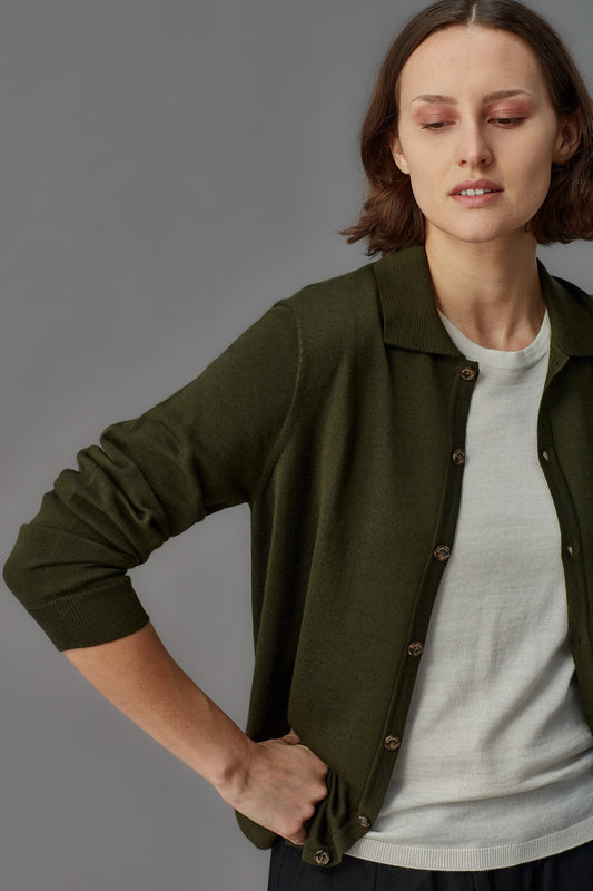Woman wearing a green jacket over a white shirt on a gray background