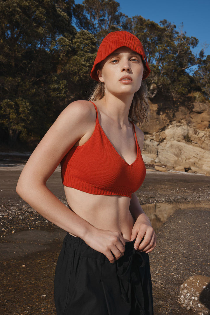 Woman wearing a red bralette and black pants standing outdoors with trees and rocks in the background