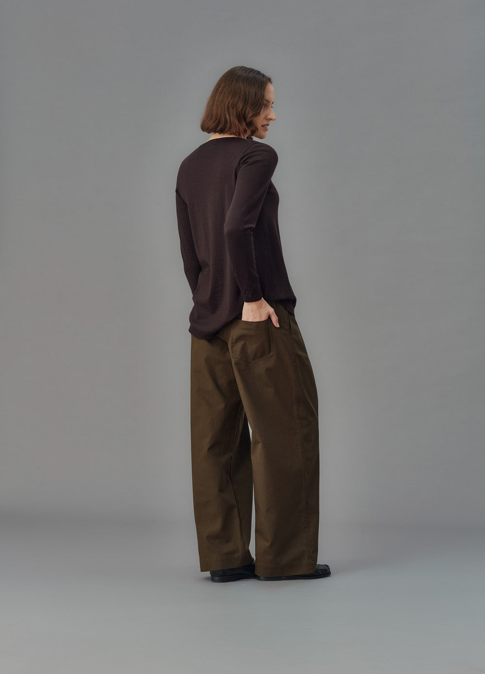 Person wearing a dark sweater and green pants against a gray background