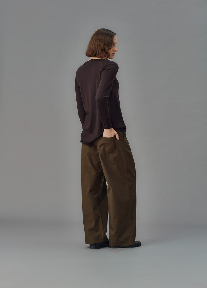 Person wearing a dark sweater and green pants against a gray background