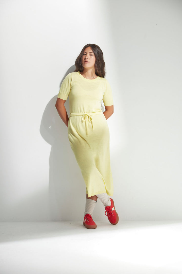 Woman wearing a yellow merino dress with red shoes against a white background