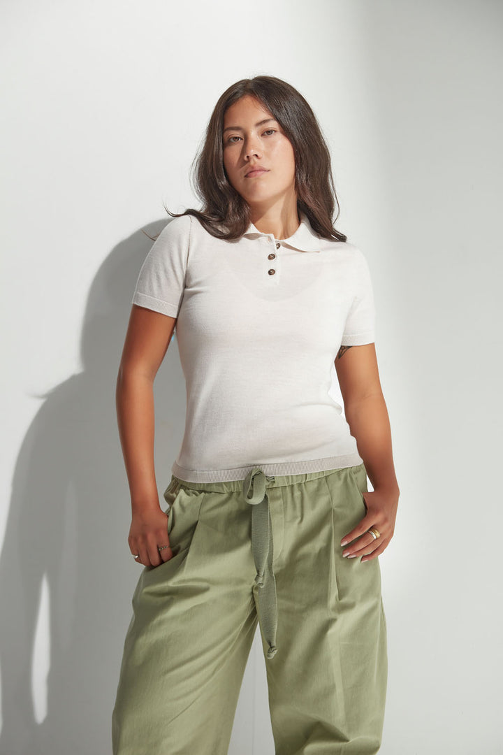 Woman wearing a white polo shirt and green pants against a plain background