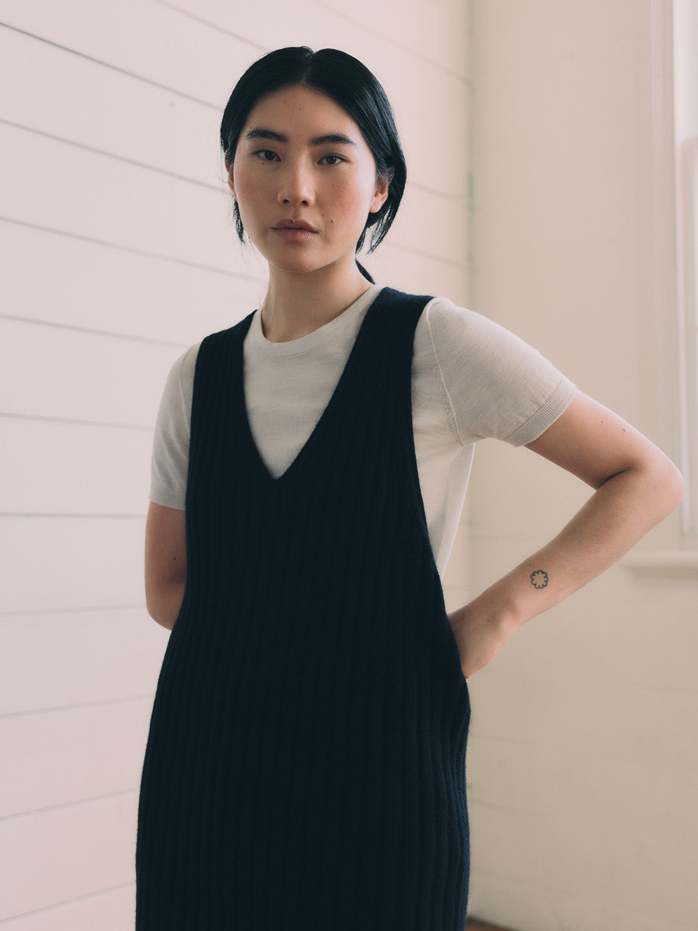 Woman wearing a black knitted vest over a white shirt against a dark background.