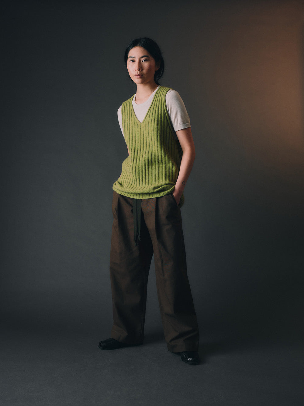 Woman wearing a green knitted vest over a white shirt against a dark background.