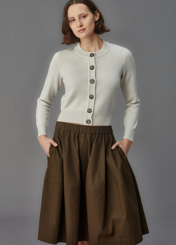 Woman wearing a alabaster cardigan and brown skirt against a gray background