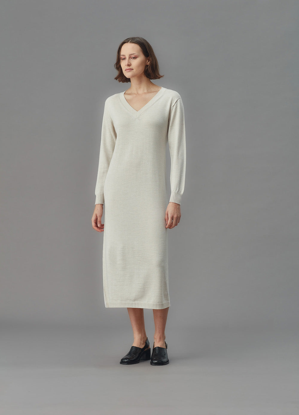 Woman wearing a long-sleeve alabaster dress against a gray background