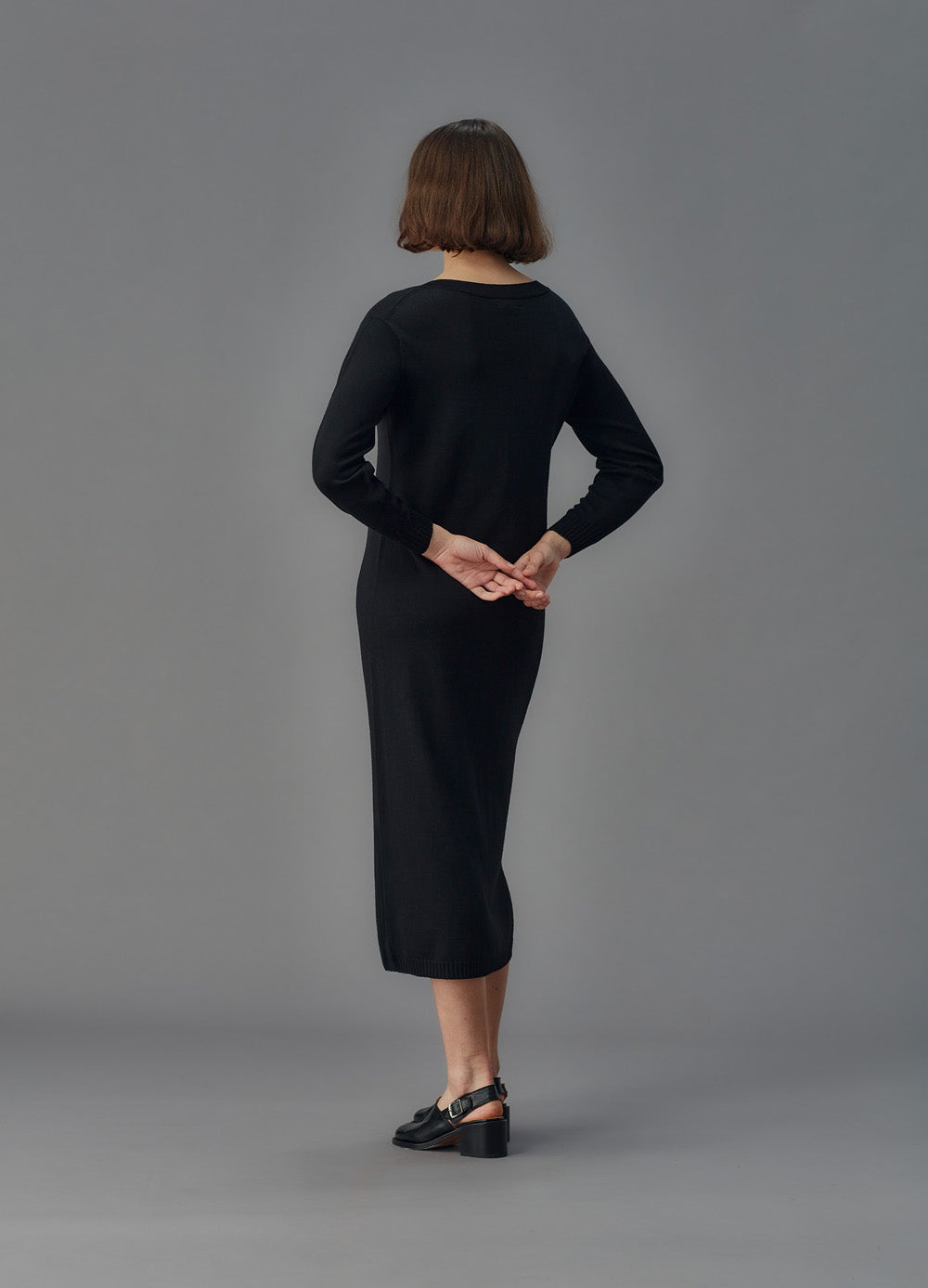 Person wearing a black dress standing against a gray background
