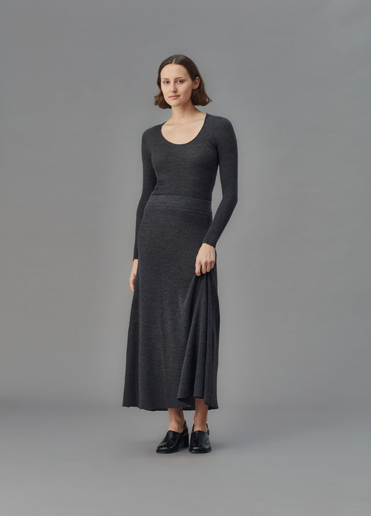 Woman wearing a long dark gray u top and skirt against a gray background