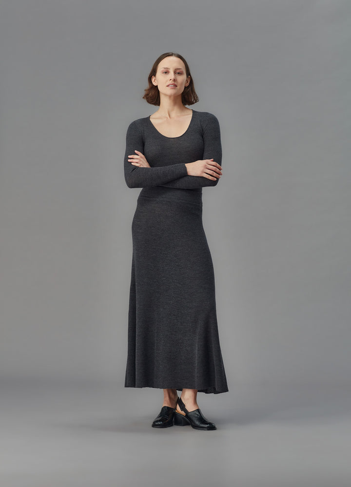 Woman wearing a long dark gray skirt and u top against a gray background