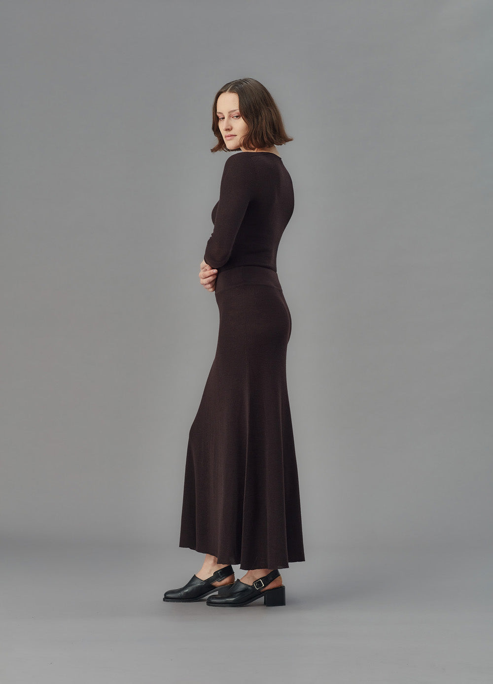 Woman wearing a long brown skirt and u top against a gray background