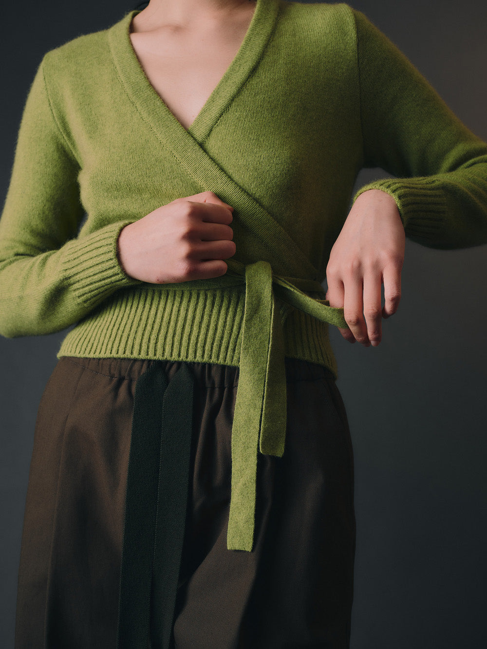 Green knitted wrap sweater with a belt worn by a woman on a dark background