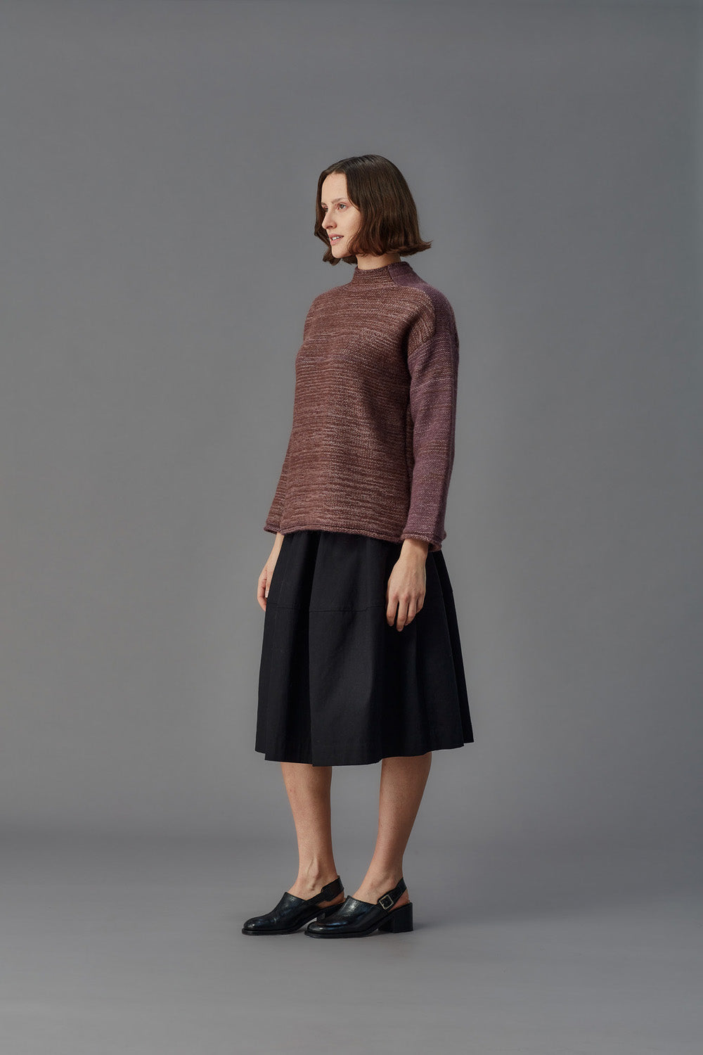 Woman wearing a maroon sweater and black skirt on a gray background