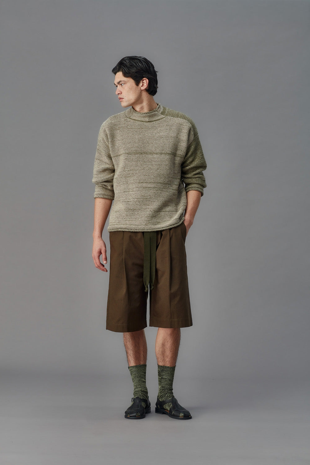 Man wearing a green sweater and brown shorts against a gray background