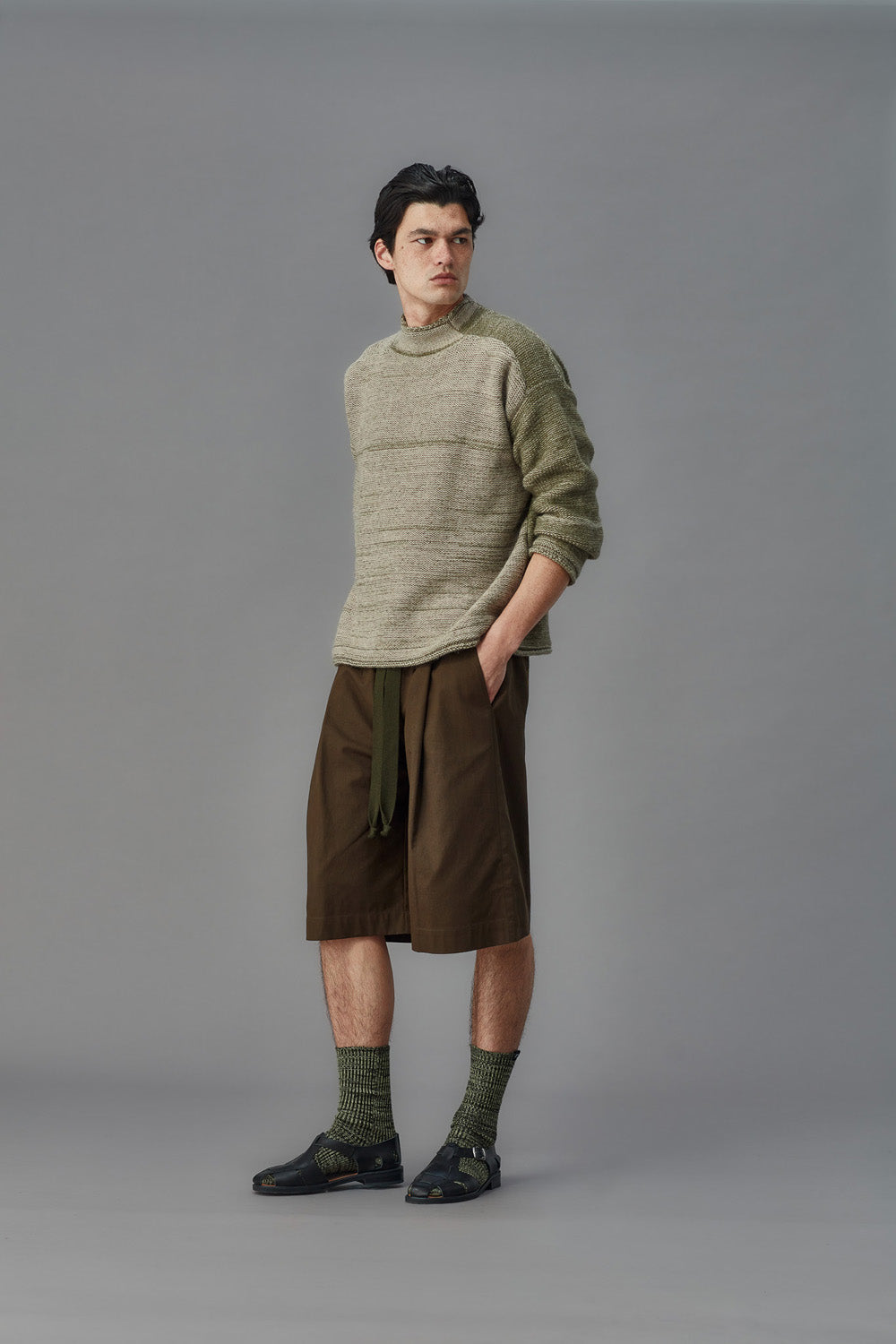 Man wearing a green sweater and brown shorts against a gray background