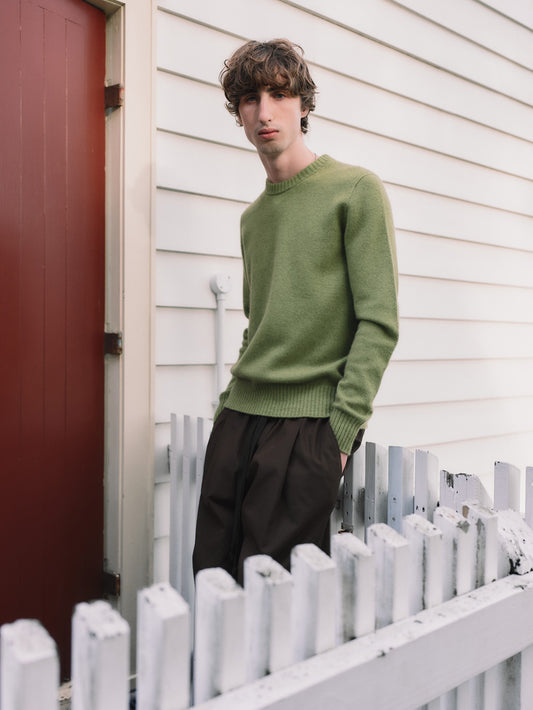 Man wearing a green sweater standing in front of a white picket fence.