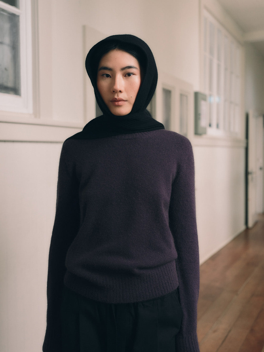 Person wearing a violet sweater and black head scarf in a hallway