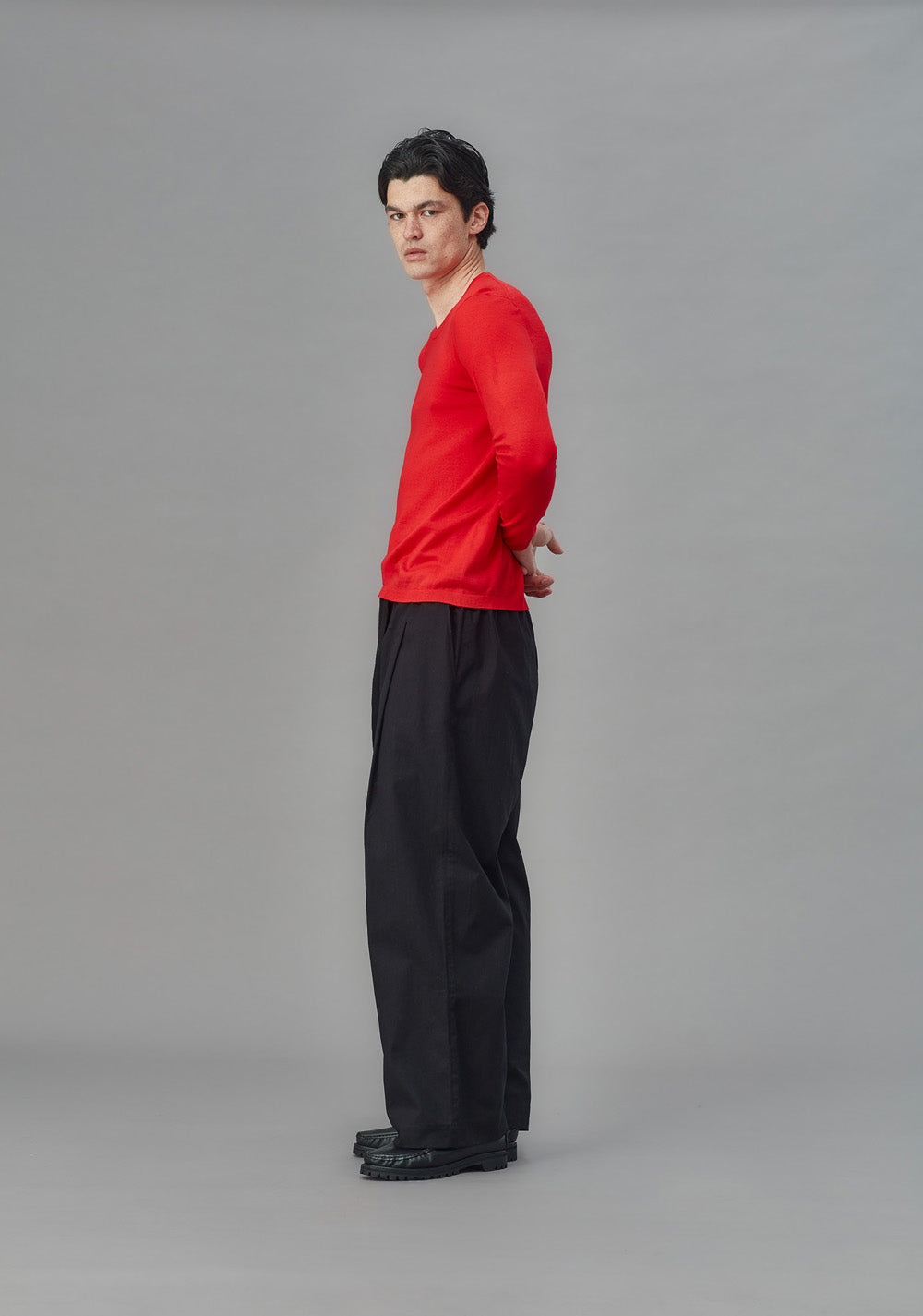 Person wearing a red sweater and black pants on a gray background