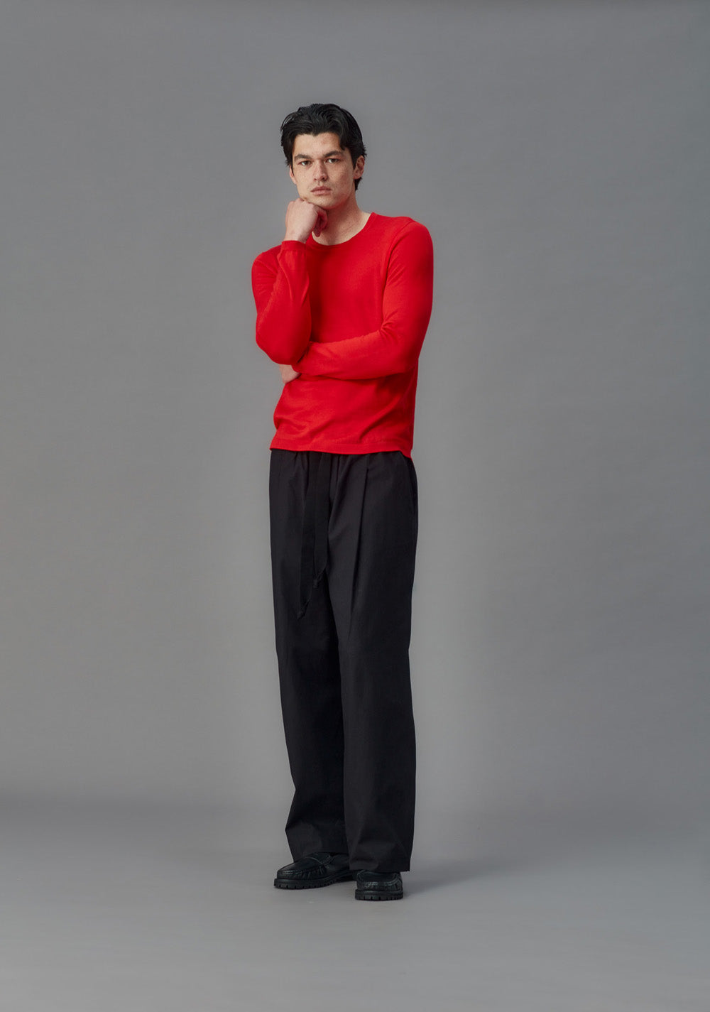 Man wearing a red sweater and black pants against a gray background