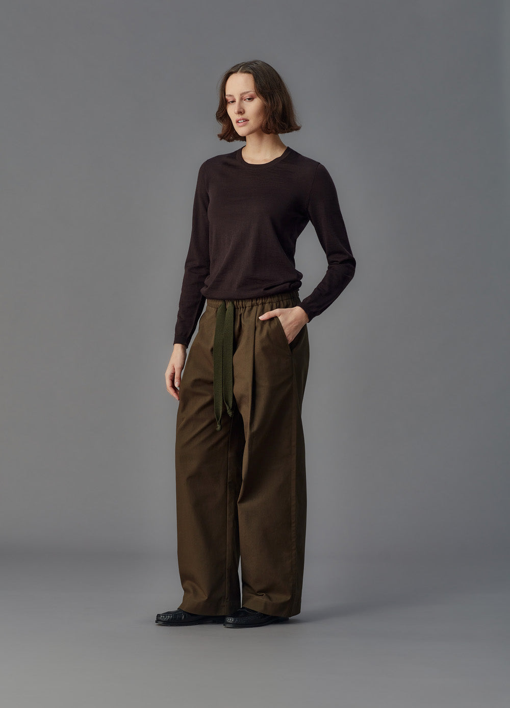 Woman wearing a brown sweater and wide-leg pants against a gray background