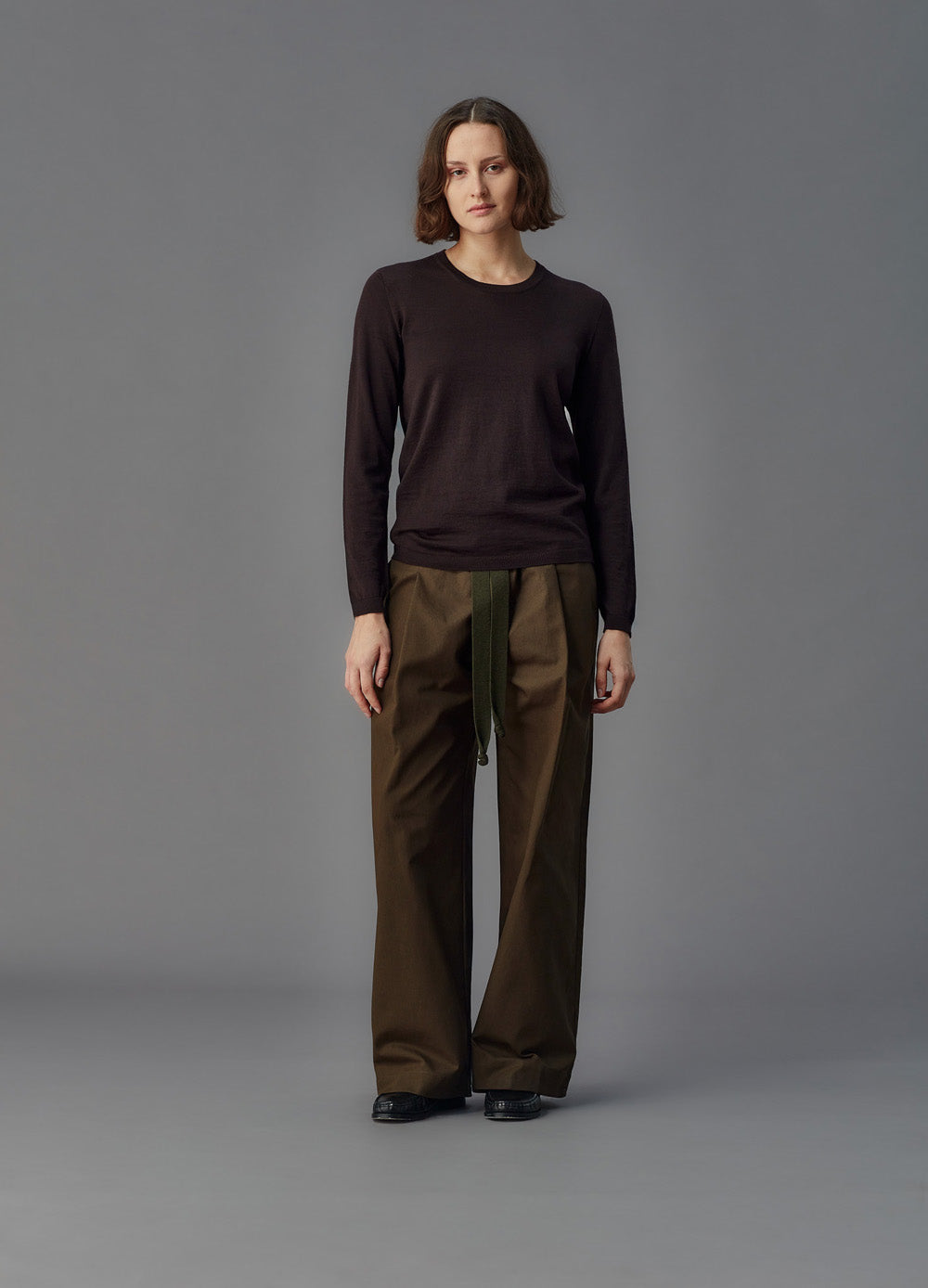 Person wearing a dark long-sleeve top and brown pants on a gray background