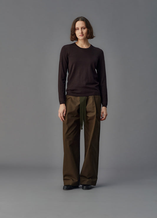 Person wearing a dark long-sleeve top and brown pants on a gray background