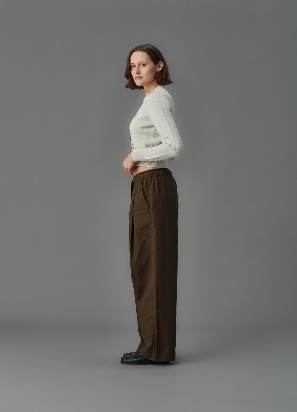 Woman wearing a alabaster white merino cardigan and brown pants on a gray background