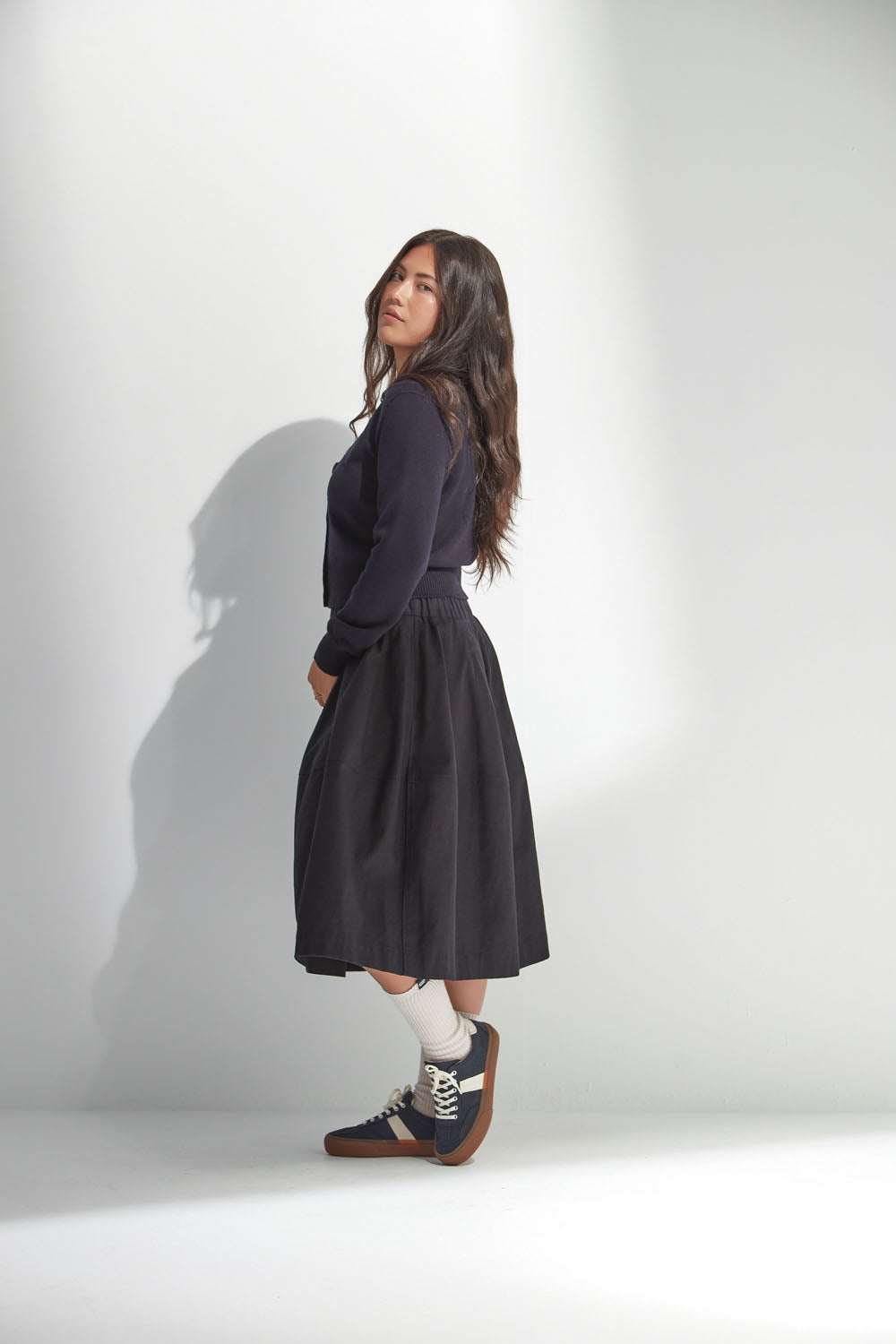Woman wearing a dark navy V Neck Cardigan with a black skirt buttons on a white background