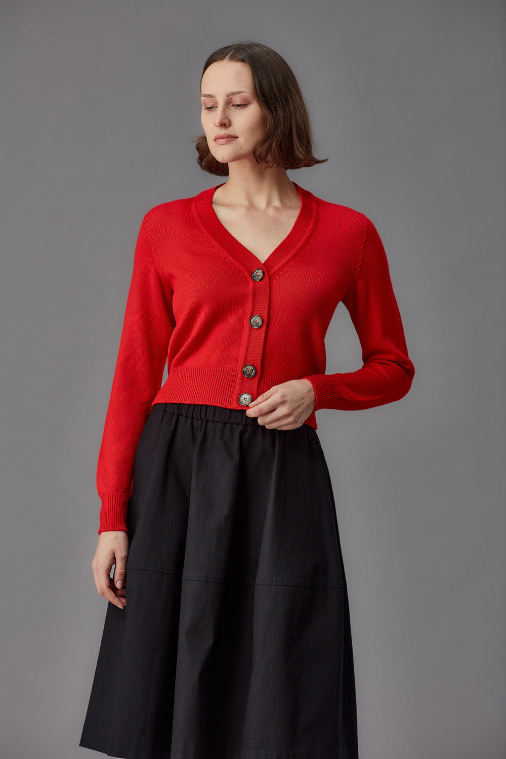 Woman wearing a red merino cardigan and brown pants on a gray background