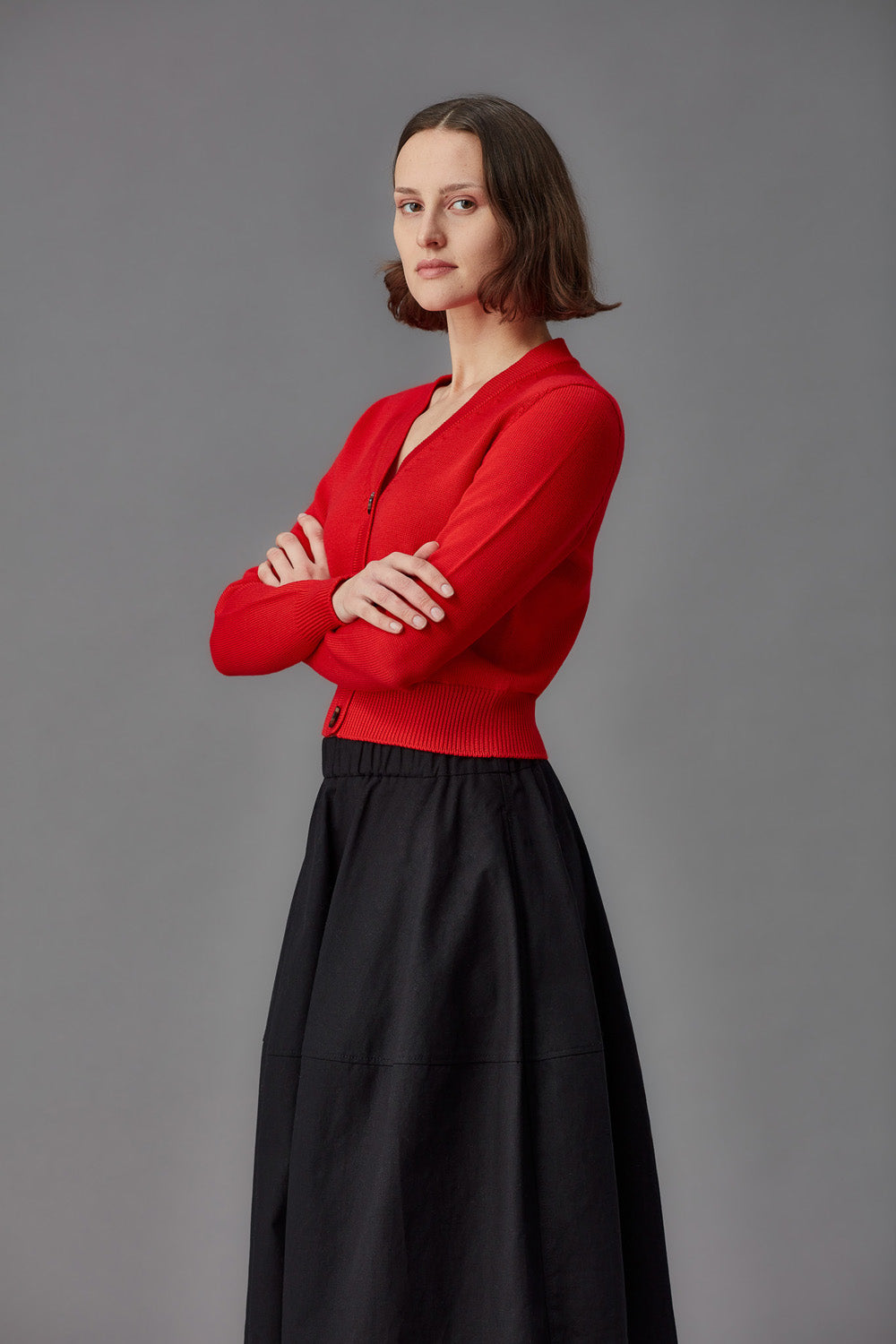 Woman wearing a red merino cardigan and brown pants on a gray background