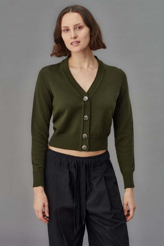 Woman wearing a green merino cardigan with buttons on a gray background